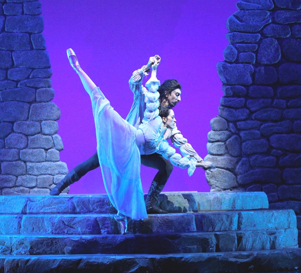 Male and Female ballerina on stage, surrounded by rock wall set and purple backdrop