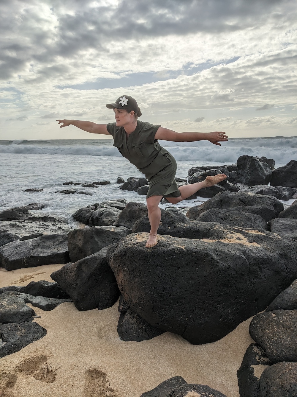 Jessica Wilson, leg in air behind, balancing on a rock in front of ocean